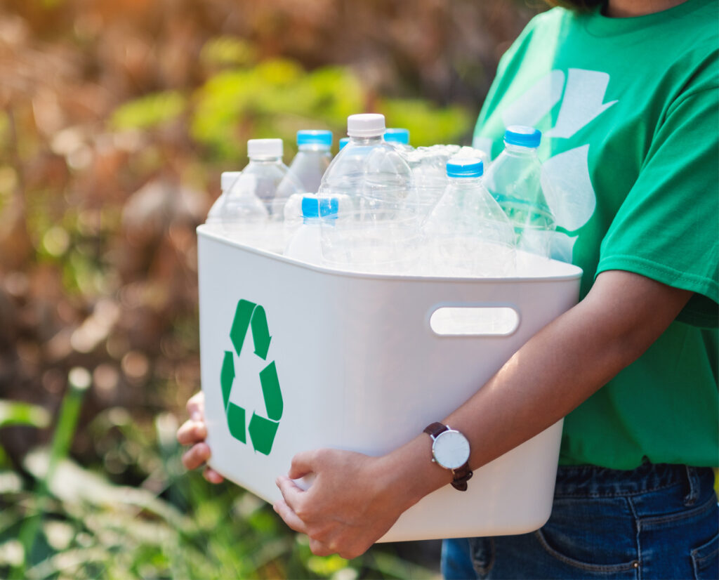 a person holding a recycling bin of plastic water bottles