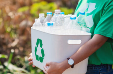 a person holding a recycling bin of plastic water bottles