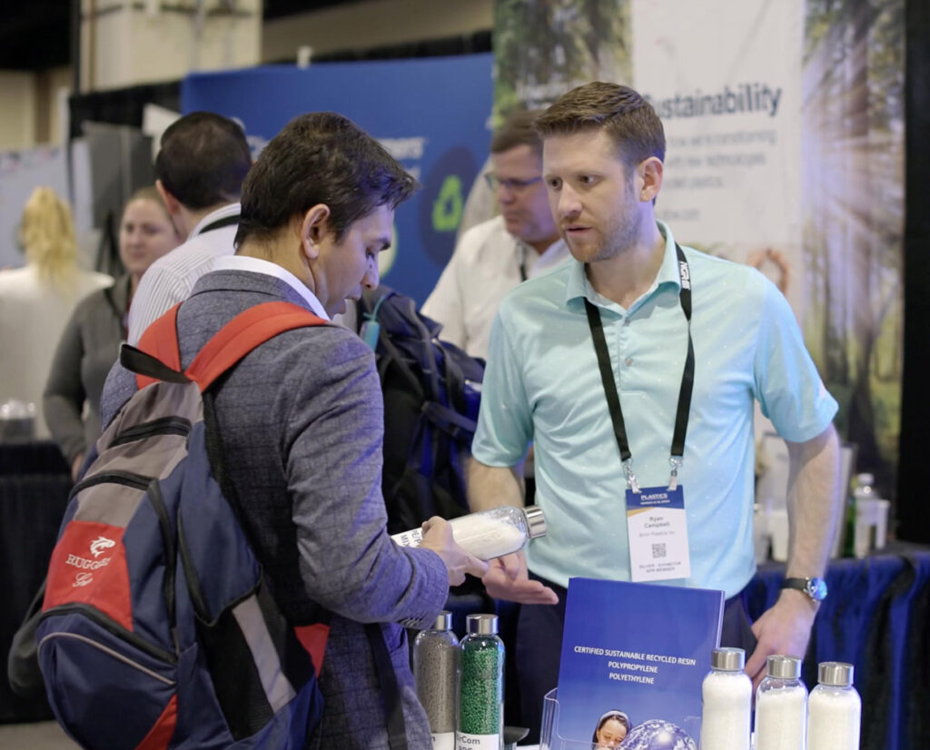 a man with a backpack on talking to a man in a blue collared shirt at a tradeshow