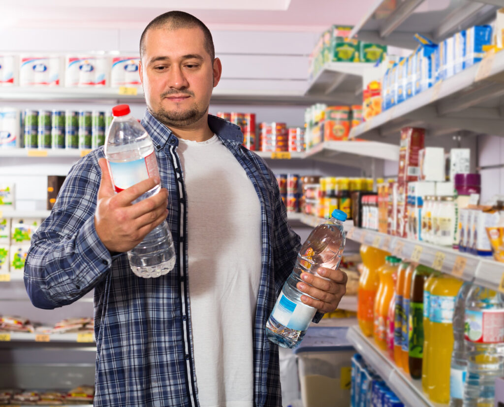 photo of a man choosing between different two water bottles in the grocery store