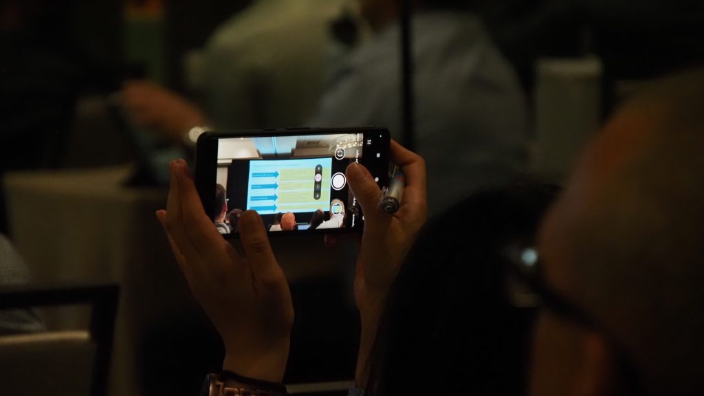 A person taking a photo of a presentation slide at an APR Member Meeting