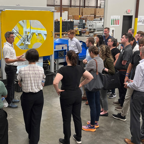 A man speaking to a small group of people in front of a piece of machinery