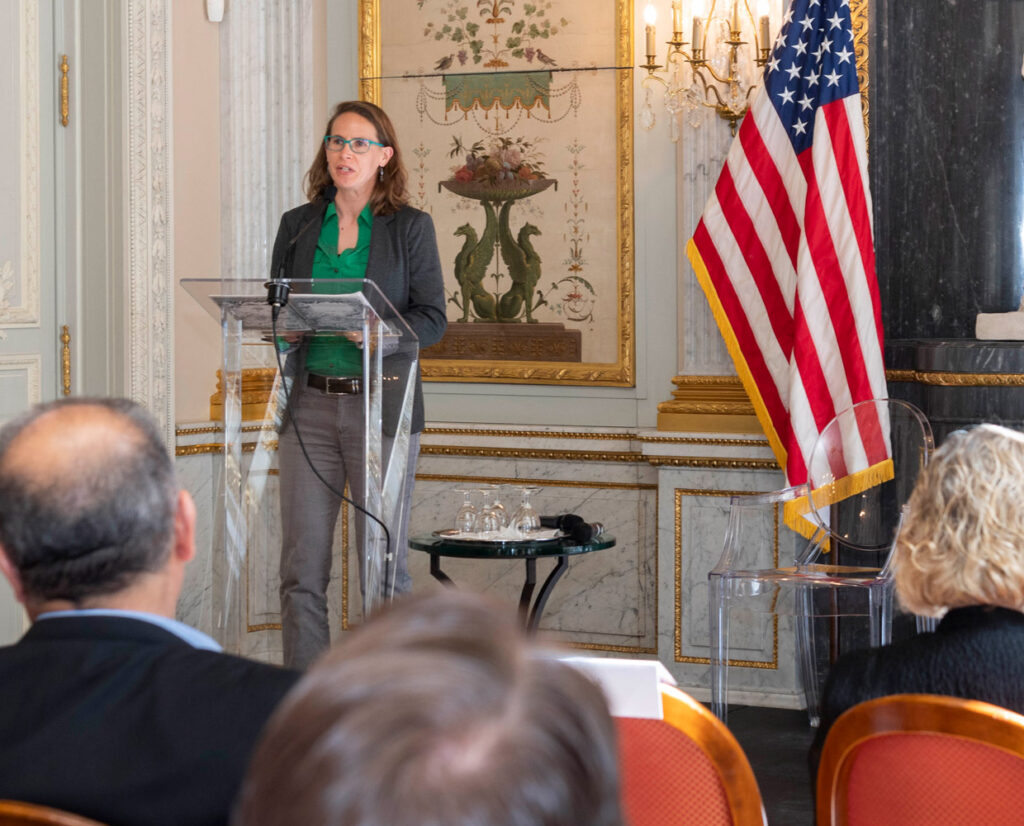 women at a podium speaking to an audience about public policy