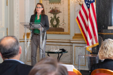 women at a podium speaking to an audience about public policy