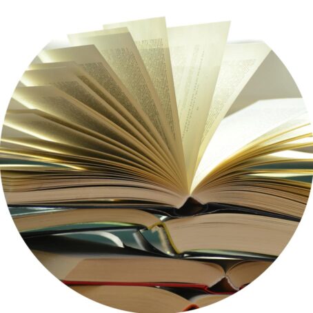 An open book with its pages being flipped, resting on top of a stack of other books.